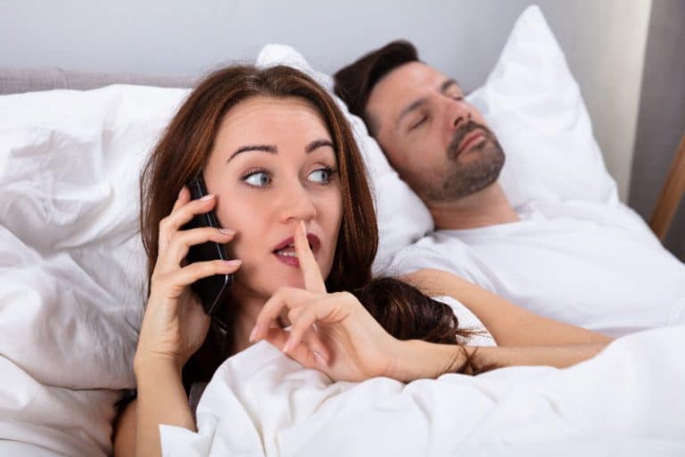 אישה מדברת בטלפון כשבעלה ישן במיטה - אישה בוגדת בבן זוג